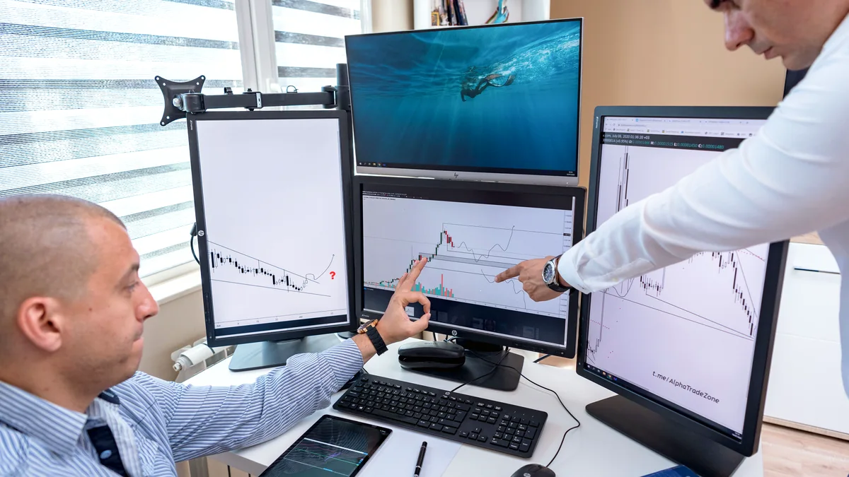 Two professionals analysing data on multiple computer screens