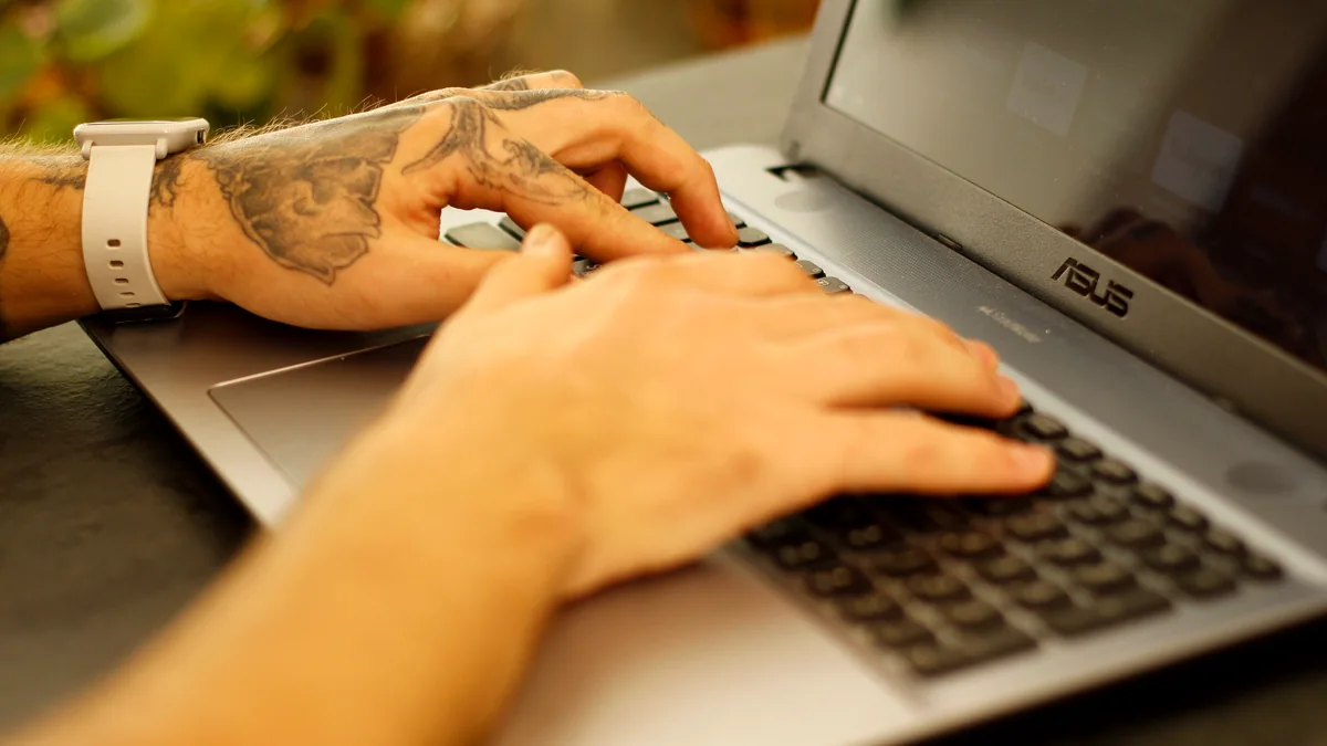 Close-up of tattooed hands typing on a laptop keyboard