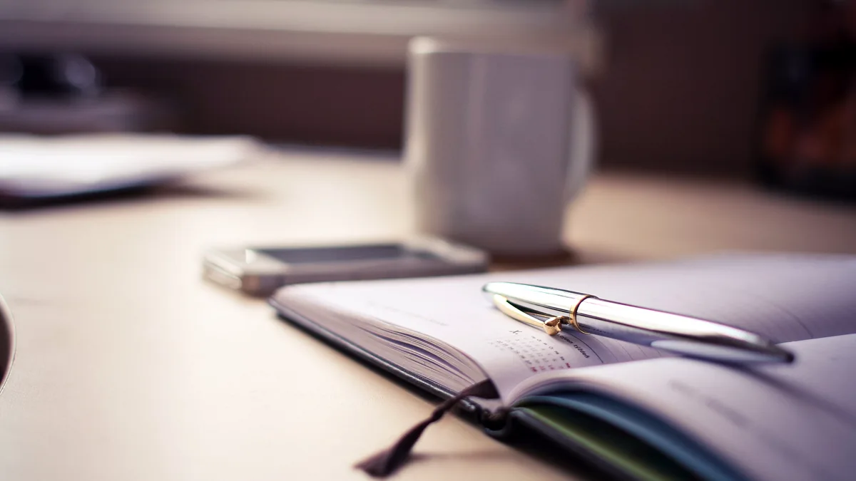 Open desk planner with a pen and coffee mug
